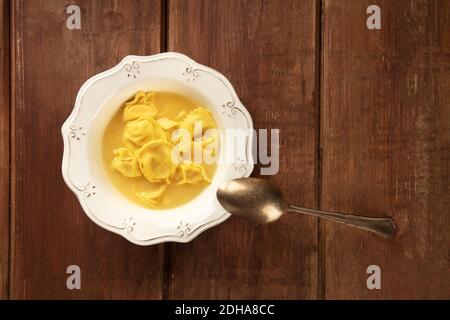 Tortellini serviti con brodo, sparati dall'alto su un rustico fondo di legno Foto Stock
