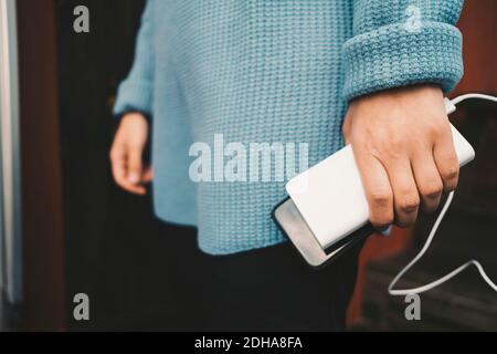 Sezione centrale di una donna che ricarica lo smartphone con un caricabatterie portatile Foto Stock