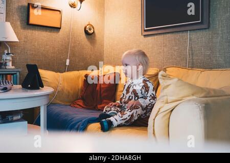 Tutta la bambina che si siede sul divano in una stanza illuminata a casa Foto Stock