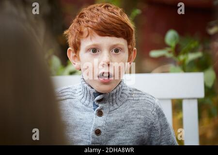 Ragazzo sorpreso che guarda via mentre si siede in cortile Foto Stock