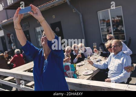 Donna anziana con amici che prendono selfie usando il telefono mobile a. patio del ristorante Foto Stock