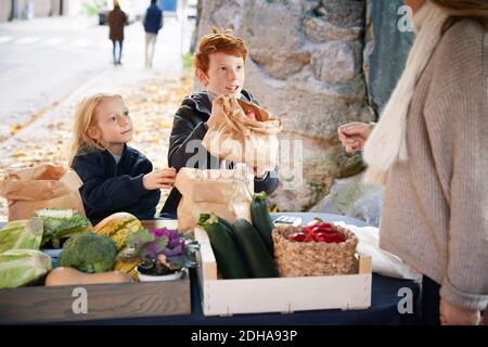 Maschio e femmina fratello che compra le verdure dal venditore di mercato femminile Foto Stock