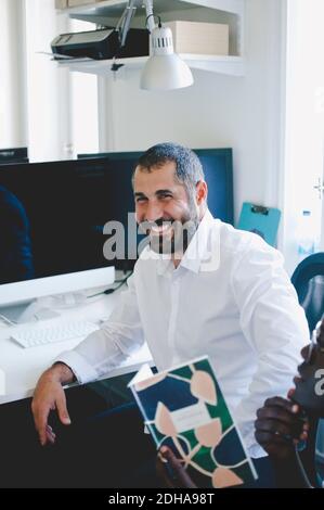 Uomo d'affari sorridente maturo seduto al tavolo in ufficio creativo Foto Stock