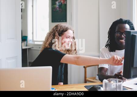 Sorridente giovane donna d'affari che mostra qualcosa al collega sul computer dentro ufficio creativo Foto Stock