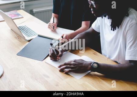 Vista ad alto angolo della gente di affari che scrive sui libri a. tavolo in ufficio creativo Foto Stock