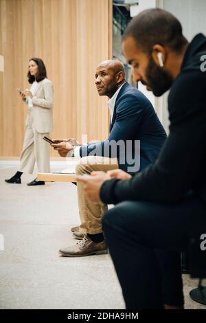 Professionisti di sesso maschile e femminile che guardano lontano mentre tengono lo smartphone fuori ufficio Foto Stock