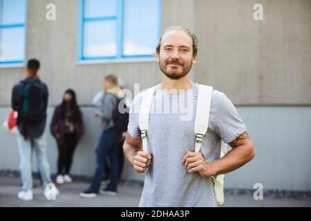 Ritratto di sorridente studente universitario al campus con amici in piedi in background Foto Stock
