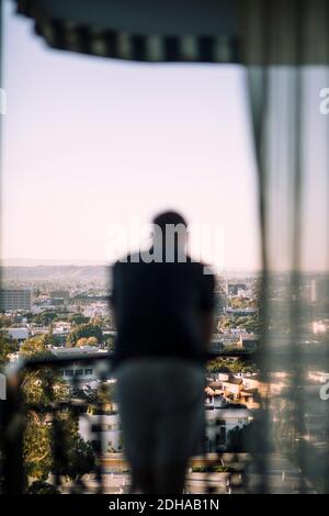 Vista posteriore di uomo maturo appoggiato su ringhiera di balcone contro città Foto Stock