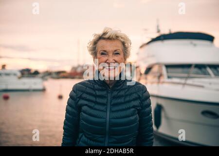 Ritratto di donna anziana felice in piedi al porto durante il tramonto Foto Stock