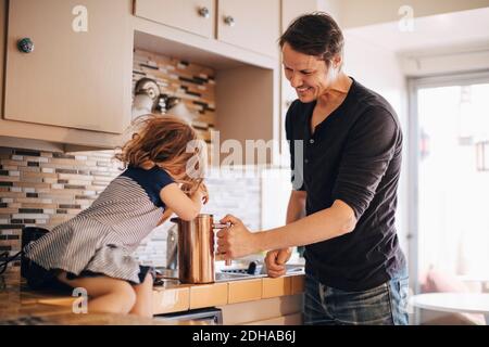 Felice padre che guarda la figlia che spinge la stampa francese mentre si siede sul banco della cucina Foto Stock