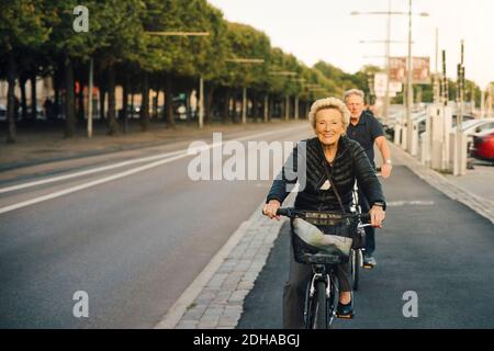 Ritratto di donna anziana sorridente con l'uomo che cavalcava le biciclette via della città Foto Stock
