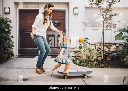 Figlia che si bilancia sullo skateboard con l'aiuto di madre sul sentiero Foto Stock