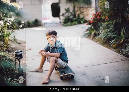 Ragazzo che guarda via mentre si siede sopra skateboard sul sentiero Foto Stock