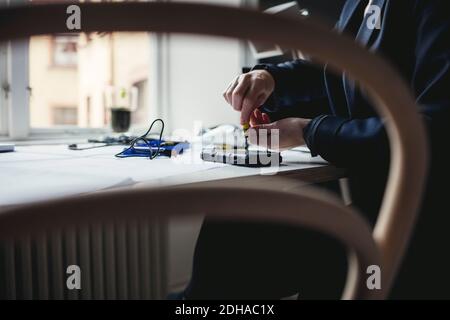 Sezione centrale del tecnico che ripara il disco rigido portatile visto attraverso la sedia in ufficio a casa Foto Stock