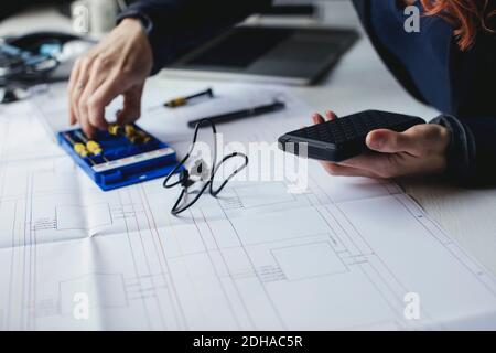 Sezione centrale del tecnico femminile che tiene il disco rigido portatile sulla scrivania Foto Stock