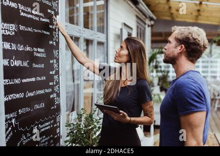 Donna d'affari con tablet digitale rivolto verso la parete mentre si sta in piedi collaboratore del ristorante Foto Stock