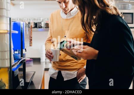 Sezione centrale di donna d'affari che versa il latte in vetro dalla scatola per uomo d'affari presso la caffetteria dell'ufficio Foto Stock