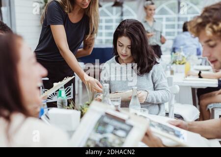 Sezione centrale del proprietario che mostra il menu alla donna seduta nel ristorante con gli amici Foto Stock