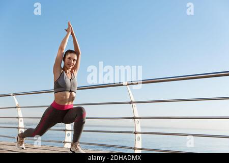 Immagine di donna in forma e fitness sana che lavora da sola vicino al mare. Donna sportiva che si allunga prima di fare jogging, facendo scaldare l'esizzatore Foto Stock