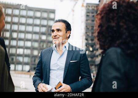 Uomo d'affari sorridente e maturo che parla con colleghi di sesso femminile in città Foto Stock