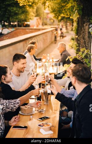 Felici amici maschi e femmine che tostano la birra mentre si siedono giardino Foto Stock