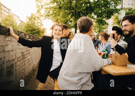Ritratto di felice giovane donna seduta con gli amici e godendosi alla riunione sociale Foto Stock