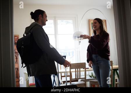 Donna sorridente che tiene le chiavi mentre parla con l'uomo in appartamento il giorno di sole Foto Stock