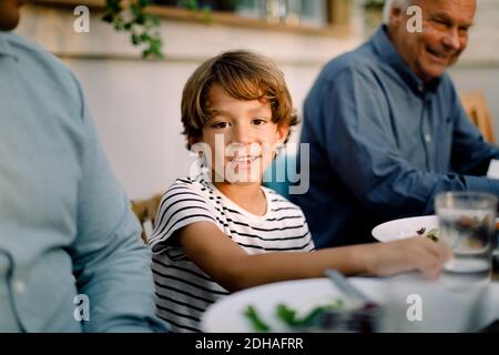Ritratto di ragazzo sorridente seduto con la famiglia al tavolo da pranzo durante il pranzo Foto Stock