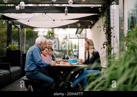 Sorridente famiglia che gioca gioco da tavolo mentre si siede al tavolo patio Foto Stock