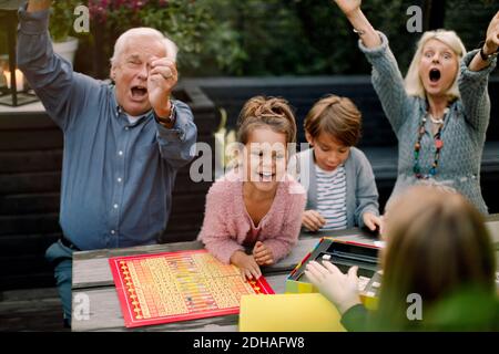 Sorridente allegro gioco da tavolo con la famiglia seduto al tavolo in cortile Foto Stock