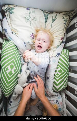 Piangendo il bambino che giace nel presepe mentre le mani del padre arrivare per lui Foto Stock