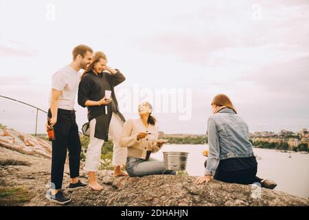 Amici felici che gustano il cibo sulla riva del lago contro il cielo Foto Stock