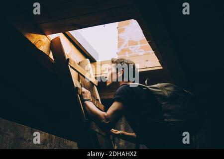 Vista laterale dello zaino da trasporto di un giovane uomo durante l'arrampicata scala verso il terrazzo Foto Stock