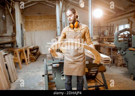 Ritratto di un bel falegname che guarda al prodotto in legno, costruendo merci con legno compensato presso l'officina Foto Stock