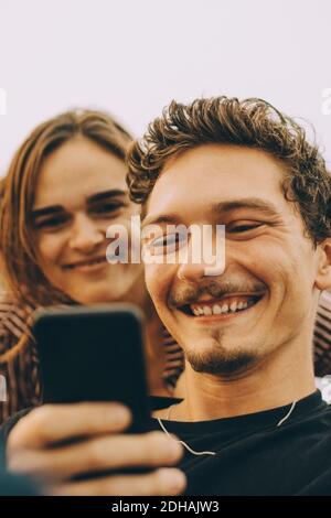 Uomo sorridente che mostra il telefono cellulare ad un amico sulla terrazza a. festa sul tetto Foto Stock