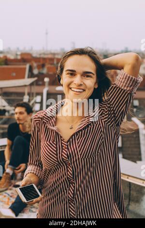 Ritratto di donna sorridente con smartphone in piedi sulla terrazza in città Foto Stock
