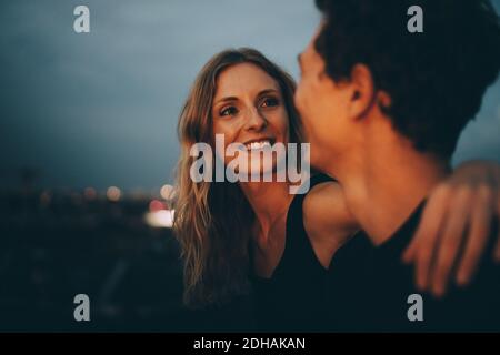Donna sorridente con braccio attorno guardando l'uomo mentre si siede sulla terrazza al tramonto Foto Stock