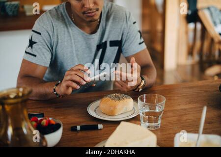 L'uomo che fa il test del diabete mentre fa la colazione al tavolo Foto Stock