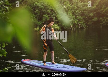 Tutta la lunghezza di sorriso donna anziana paddleboarding in mare durante Corso SUP Foto Stock