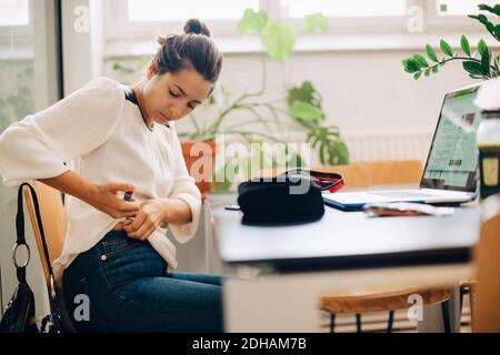 Donna d'affari che inietta l'insulina mentre si siede alla scrivania in ufficio Foto Stock