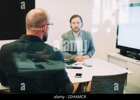 I colleghi di lavoro che discutono durante una riunione vista attraverso il vetro in ufficio Foto Stock