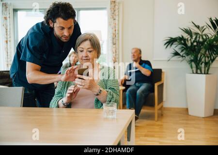Uomo sicuro che assiste donna anziana utilizzando smartphone in casa di cura Foto Stock