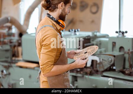 Un falegname lavora su una macchina per la lavorazione del legno, tenendo la taglierina in officina Foto Stock