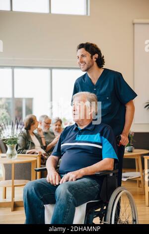 Sorridente infermiera maschio che spinge l'uomo anziano disabile sulla sedia a rotelle a. casa di riposo Foto Stock