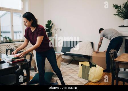 Donna che organizza i libri sul tavolo mentre disimballano le scatole in vita camera nella nuova casa Foto Stock