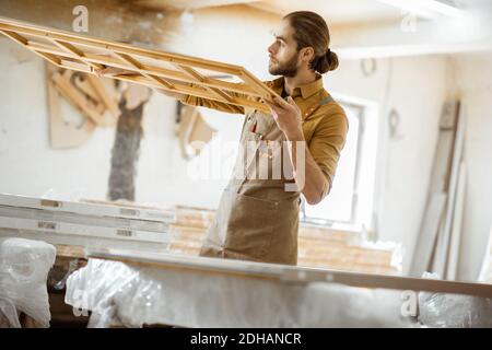 Bel falegname che controlla la qualità del telaio della finestra prima la vernice presso l'officina di falegnameria Foto Stock