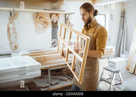 Bel falegname che controlla la qualità del telaio della finestra prima la vernice presso l'officina di falegnameria Foto Stock