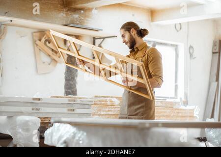 Bel falegname che controlla la qualità del telaio della finestra prima la vernice presso l'officina di falegnameria Foto Stock