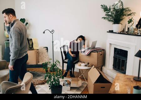 Uomo che parla sul telefono cellulare e donna che usa il computer portatile a. nuova casa Foto Stock