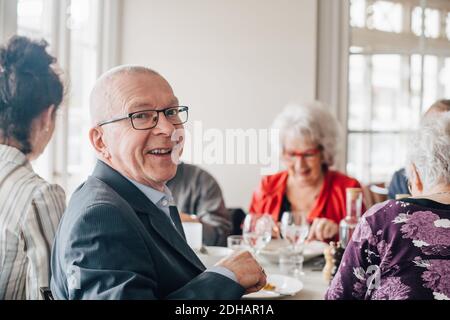 Ritratto dell'uomo anziano sorridente mentre si siede da amici dentro ristorante Foto Stock
